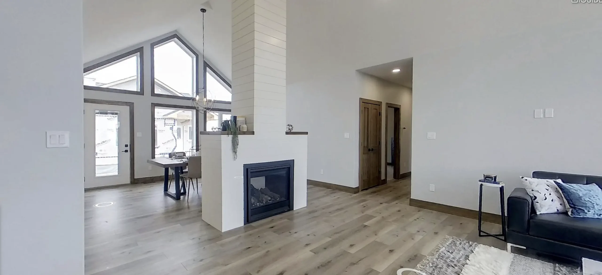 RTM home in Alberta or Saskatchewan with a central two sided fireplace wrapped in shiplap, vaulted ceiling, triangular windows, light wood floors, dining area, and a dark sofa.